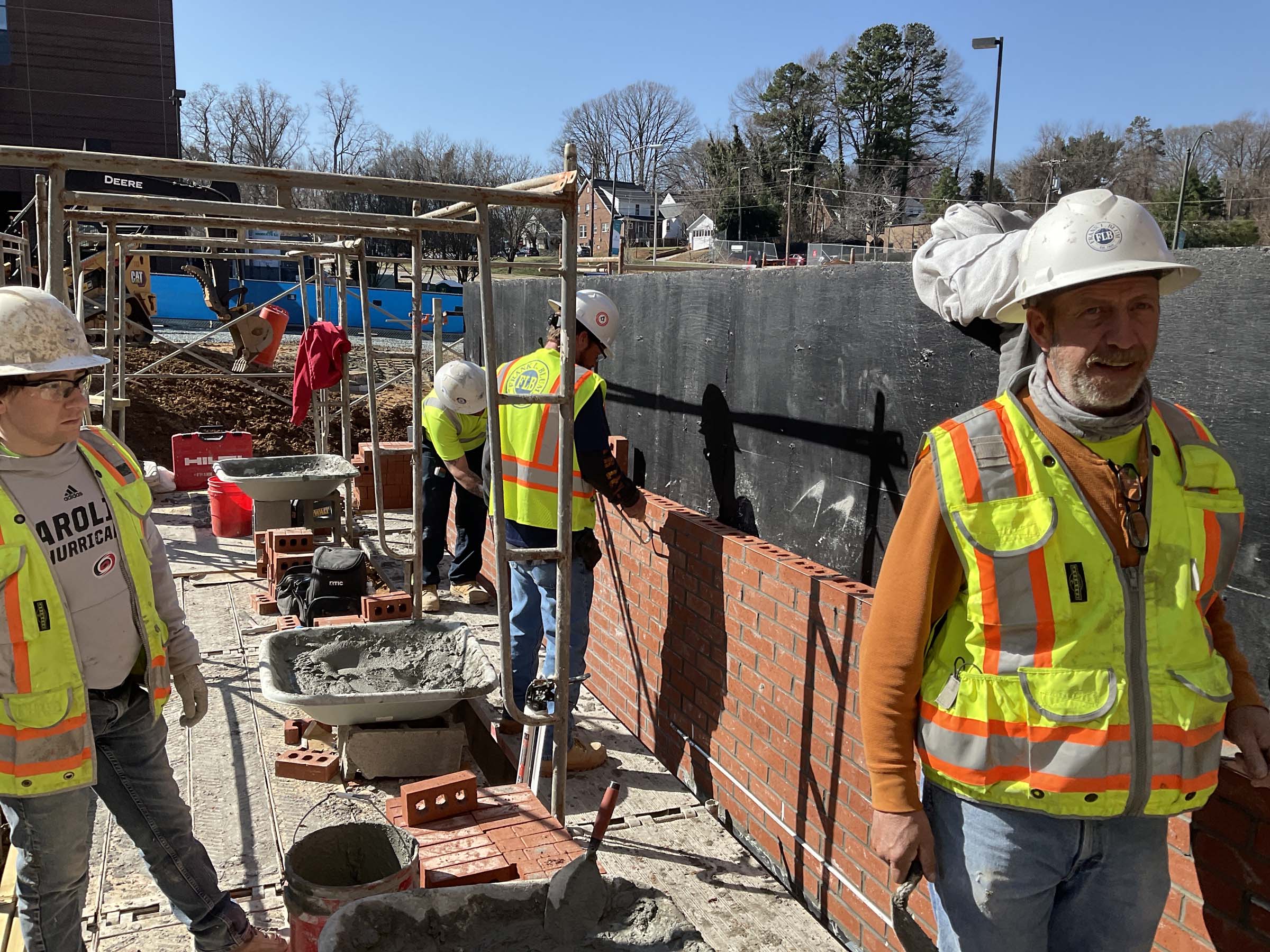 Blum Construction workers wear hi-vis vests and hardhats working with scaffolding and masonry according to OSHA guidelines on a construction site.